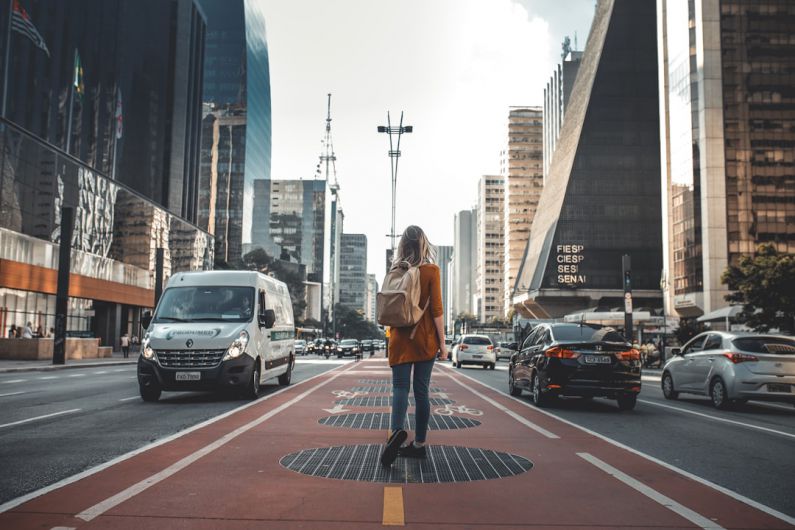 Traveler - photography of woman walking in between road with vehicles