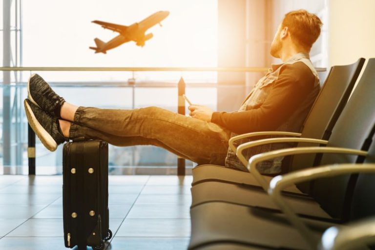 Traveler - man sitting on gang chair with feet on luggage looking at airplane