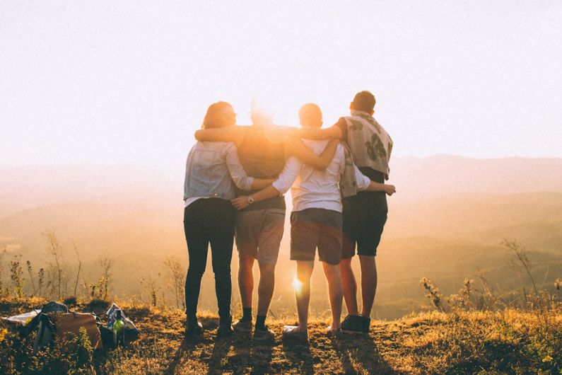 Family Fun - four person hands wrap around shoulders while looking at sunset