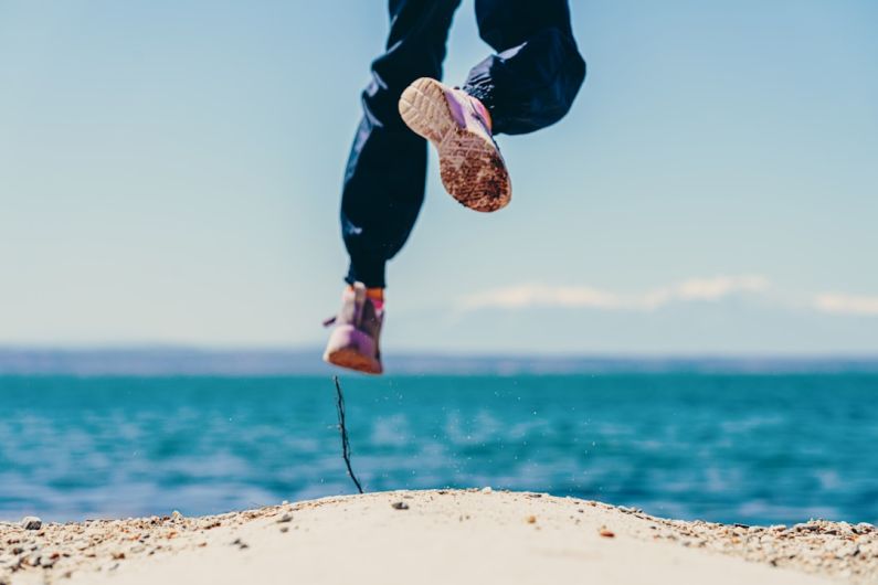 Activities - person in black pants and brown shoes jumping on brown rock near body of water during