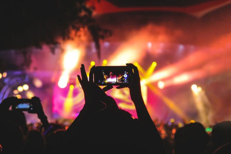 Event - person holding smartphone taking video of a concert near stage with lights during nighttime